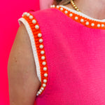 Zoomed-in image focusing on the pearl embellishments and orange/white striped neckline and sleeve hemline.