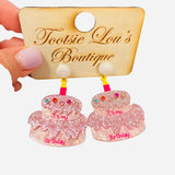 Pink glitter tiered cake earrings with rhinestone sprinkles and pearly frosting details.