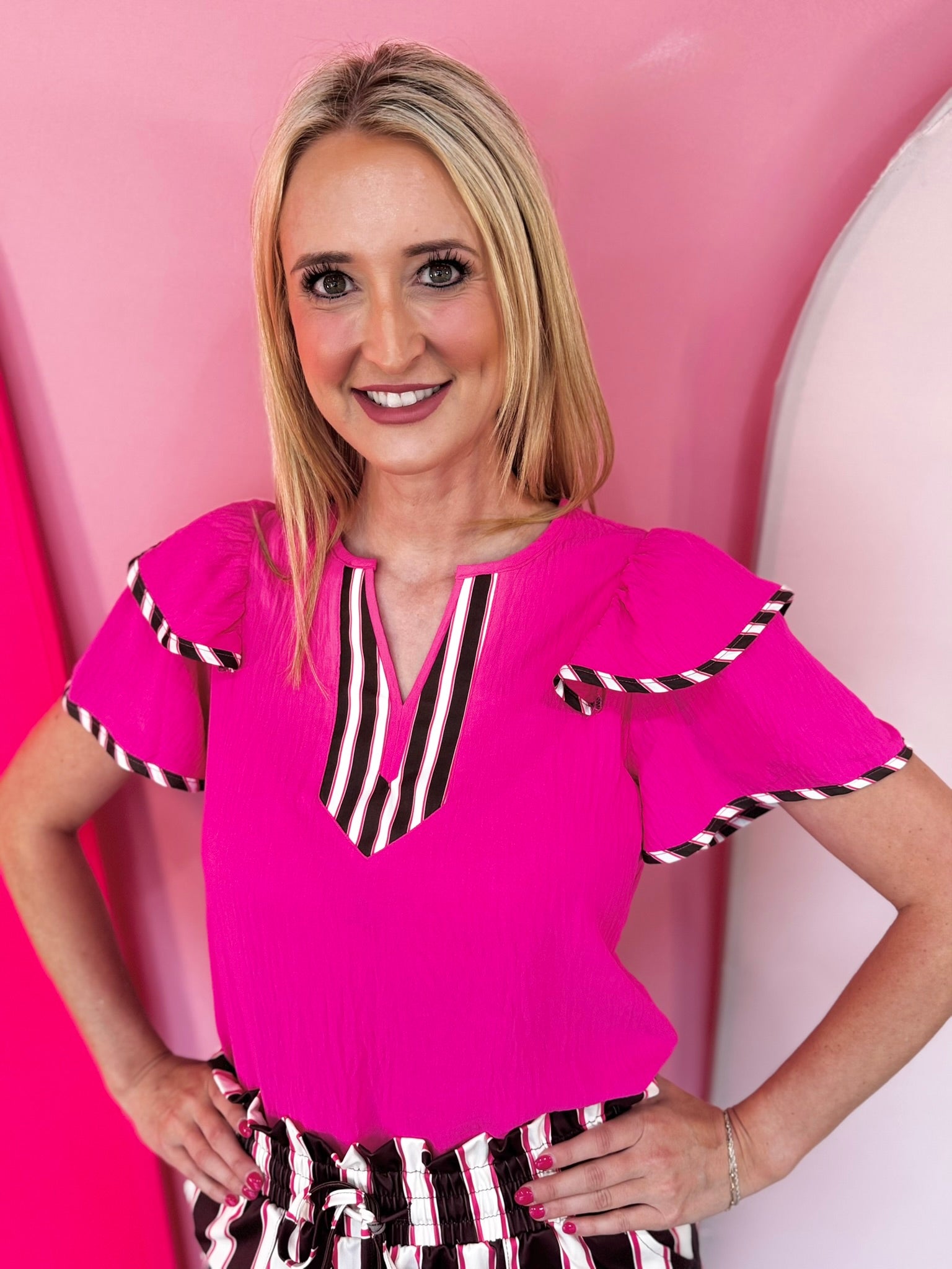 Neon pink flutter sleeve blouse with colorful striped neckline and sleeve trim.