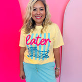 Yellow tee with alligator graphic, blue stripes, and pink “later” text.