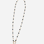 Gold chain necklace with spaced black beads and crystal-accented textured ring charm.