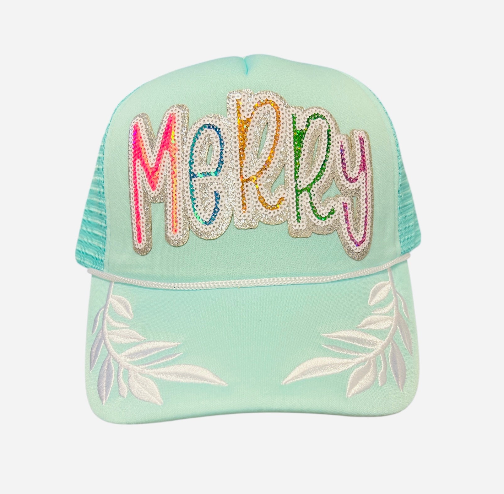 Mint trucker hat with colorful sequin “Merry” patch and white embroidered leaf accents on brim.