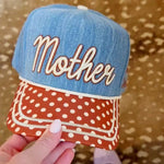 Denim “Mother Knows Best” trucker hat with rust brim, polka dots, and embroidered back icons.