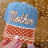 Denim “Mother Knows Best” trucker hat with rust brim, polka dots, and embroidered back icons.