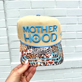 Motherhood trucker hat with tan crown, corduroy details, leopard bill, and “raising wild things” embroidery.