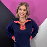 Navy half-zip pullover with vibrant pink and orange plaid neckline and cuff accents.
