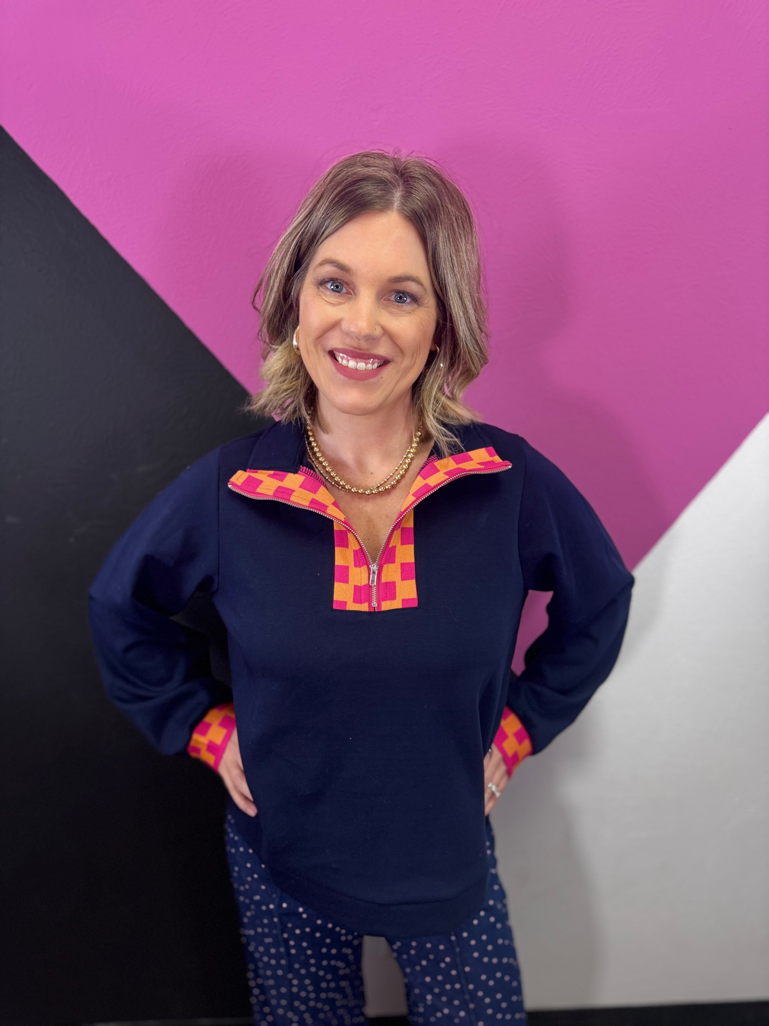 Navy half-zip pullover with vibrant pink and orange plaid neckline and cuff accents.