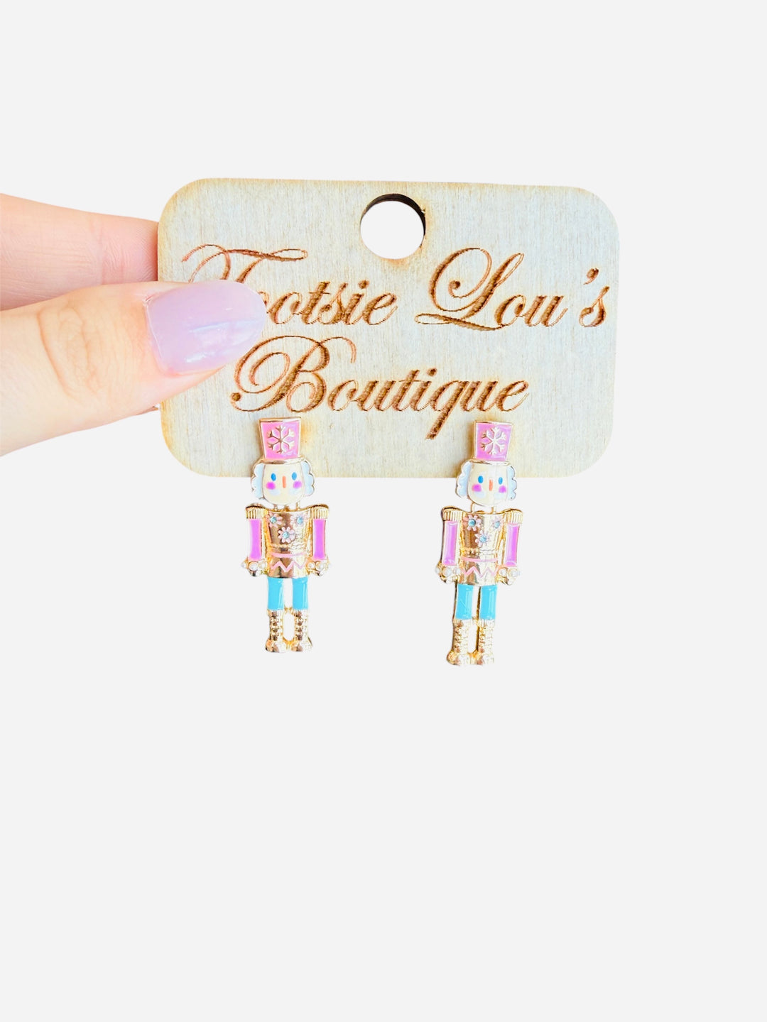 Pastel nutcracker earrings with pink hats, teal pants, gold sparkle trim, and cheerful faces.