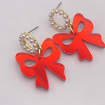 Glossy red acrylic bow earrings with pearl-beaded hoop studs, lightweight and hypoallergenic.