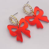 Glossy red acrylic bow earrings with pearl-beaded hoop studs, lightweight and hypoallergenic.