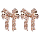 Gold bow stud earrings with rhinestones and centered faux pearl.