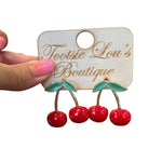 Enamel red cherry stud earrings that dangle with green leaves and gold stems.