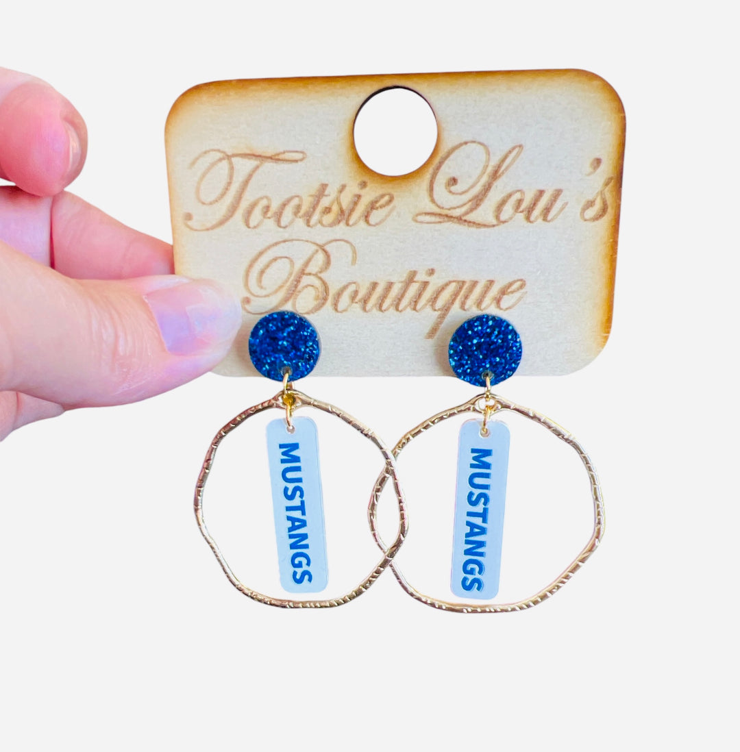 White dangle earrings with bold blue MUSTANGS lettering, glitter blue stud, and gold circle frame—perfect for spirited game day looks