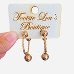 A pair of textured gold hoop earrings, each featuring a small, shiny gold sphere charm dangling from the bottom of the hoop.