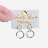 A pair of silver earrings, each featuring two interlinked hoops. Both hoops are adorned with a detailed, textured beaded pattern.