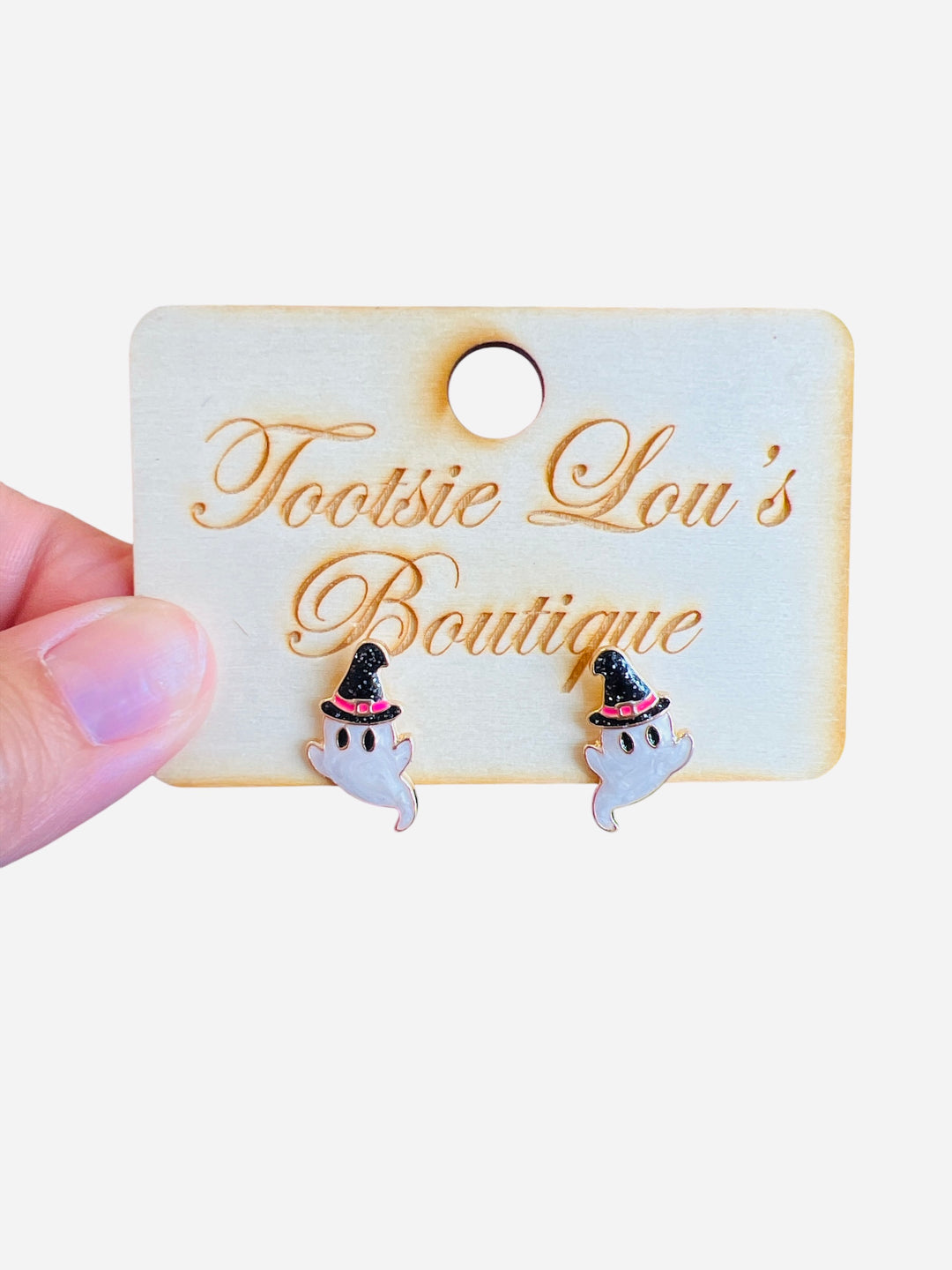 A pair of stud earrings shaped like small, white cartoon ghosts. Each ghost is wearing a glittery black witch hat that has a small pink accent band.