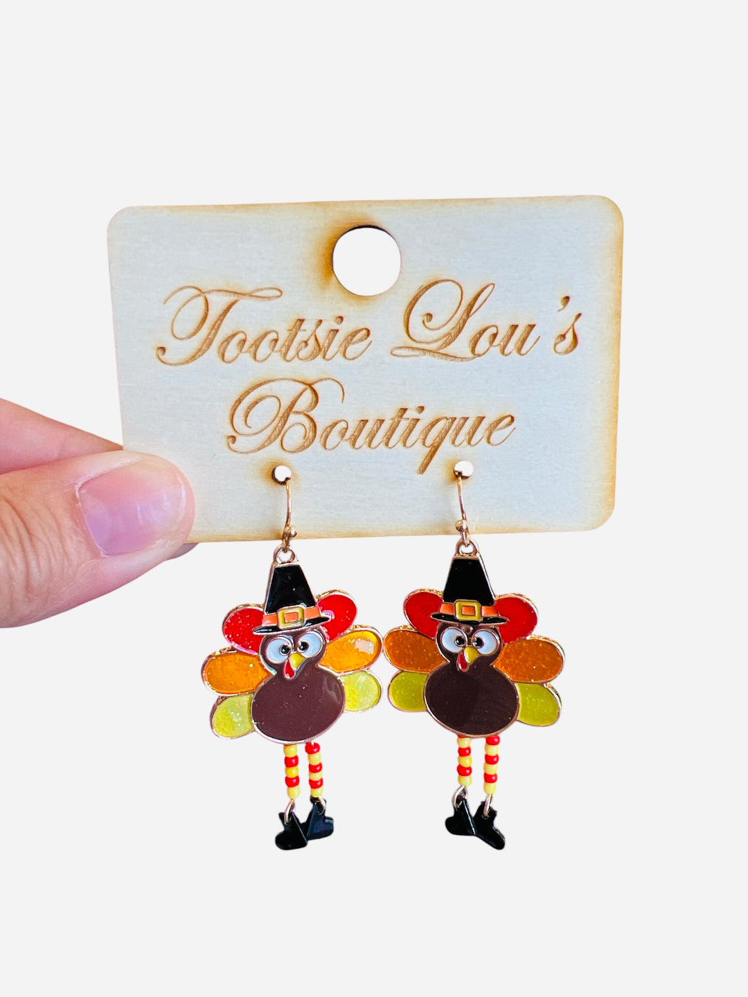 A pair of dangle earrings shaped like turkeys. The turkeys have colorful enamel tail feathers, are wearing small black pilgrim hats, and have little legs that dangle.