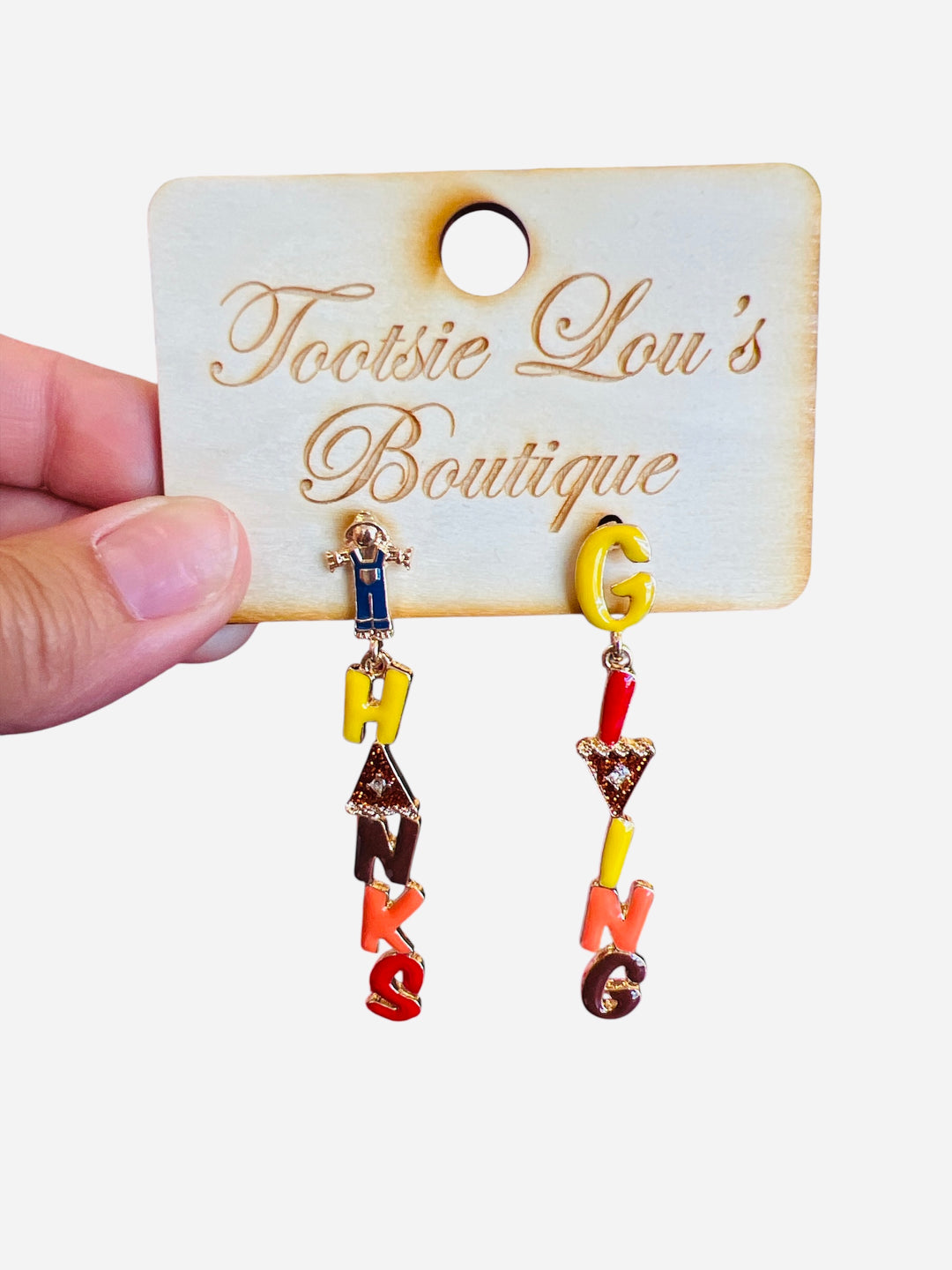 A pair of dangle earrings with letter charms. One earring's charms spell out "THANKS" and the other spells out "GIVING" in fall colors, with a small scarecrow charm at the bottom of each.