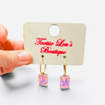 Gold-tone hoop earrings with faceted rectangular crystals reflecting iridescent pink tones.