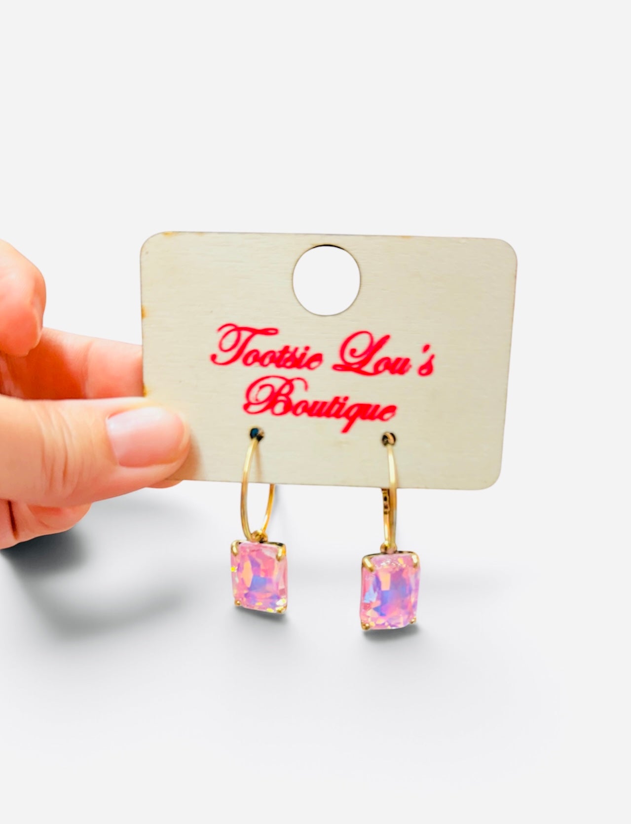 Gold-tone hoop earrings with faceted rectangular crystals reflecting iridescent pink tones.