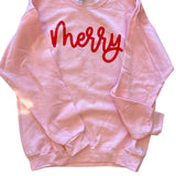Soft pink sweatshirt with bold red “Merry” script lettering in festive holiday style.