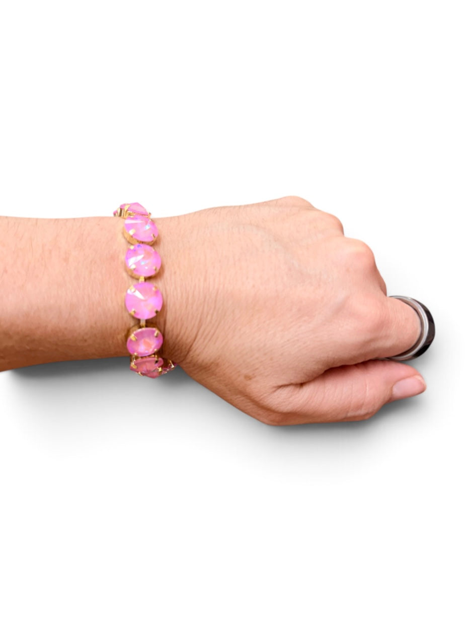 Pink opaque crystal tennis bracelet with oversized iridescent stones and gold-tone settings.