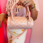 Pink polka dot crossbody bag with adjustable strap and top handles.