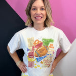 White cropped football tee with colorful game day collage, foam finger, stadium, and pennants.