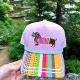 Lavender hat with embroidered dachshund, colorful sunglasses, mixed-print bill, and aqua piping.