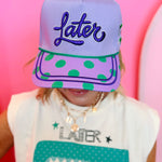 Lavender hat with green polka dot brim, alligator graphic, and “Later” embroidery.