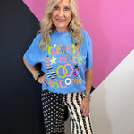 Blue graphic tee with colorful Good To Come lettering, stripes, checks, stars, and playful patterns.