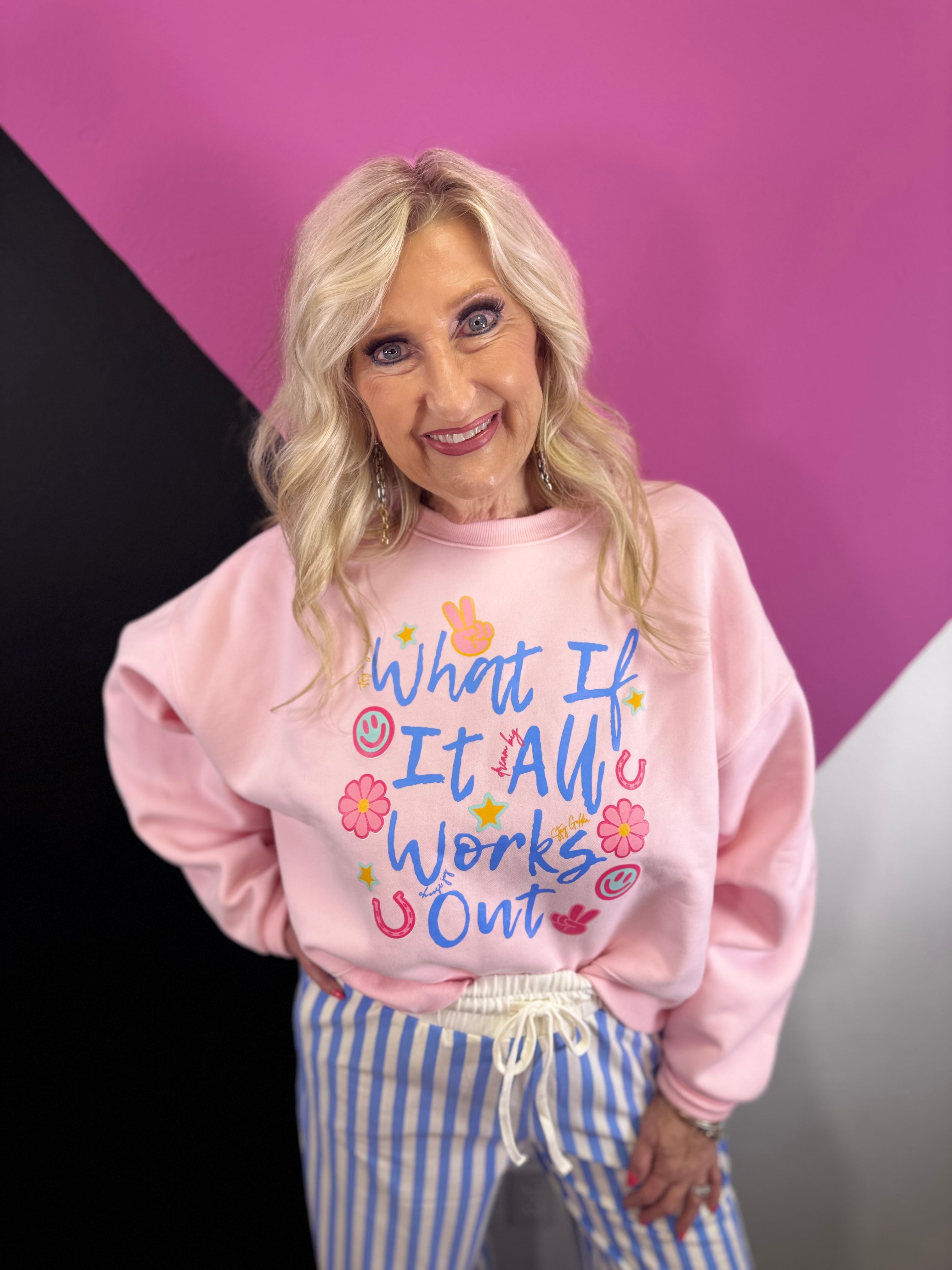 Pink sweatshirt with colorful What If It All Works Out graphic and playful icons.