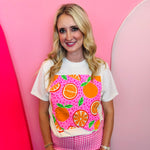 Cream tee with bright orange fruit graphic and bold pink design accents.