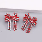 Red enamel bow stud earrings with pearl details and sparkling green rhinestone accents.