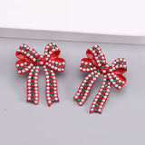 Red enamel bow stud earrings with pearl details and sparkling green rhinestone accents.