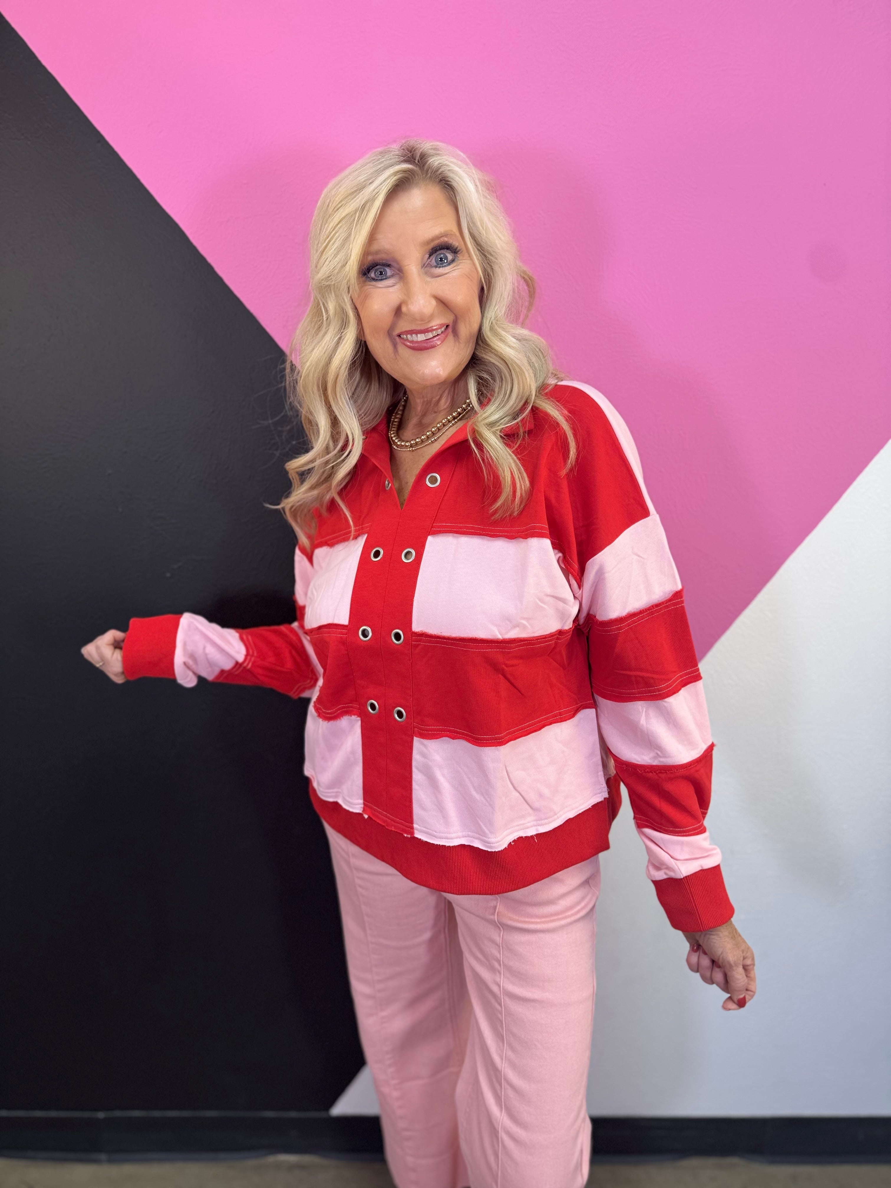 Red and pink striped pullover with grommet neckline, exposed seams, and long sleeves