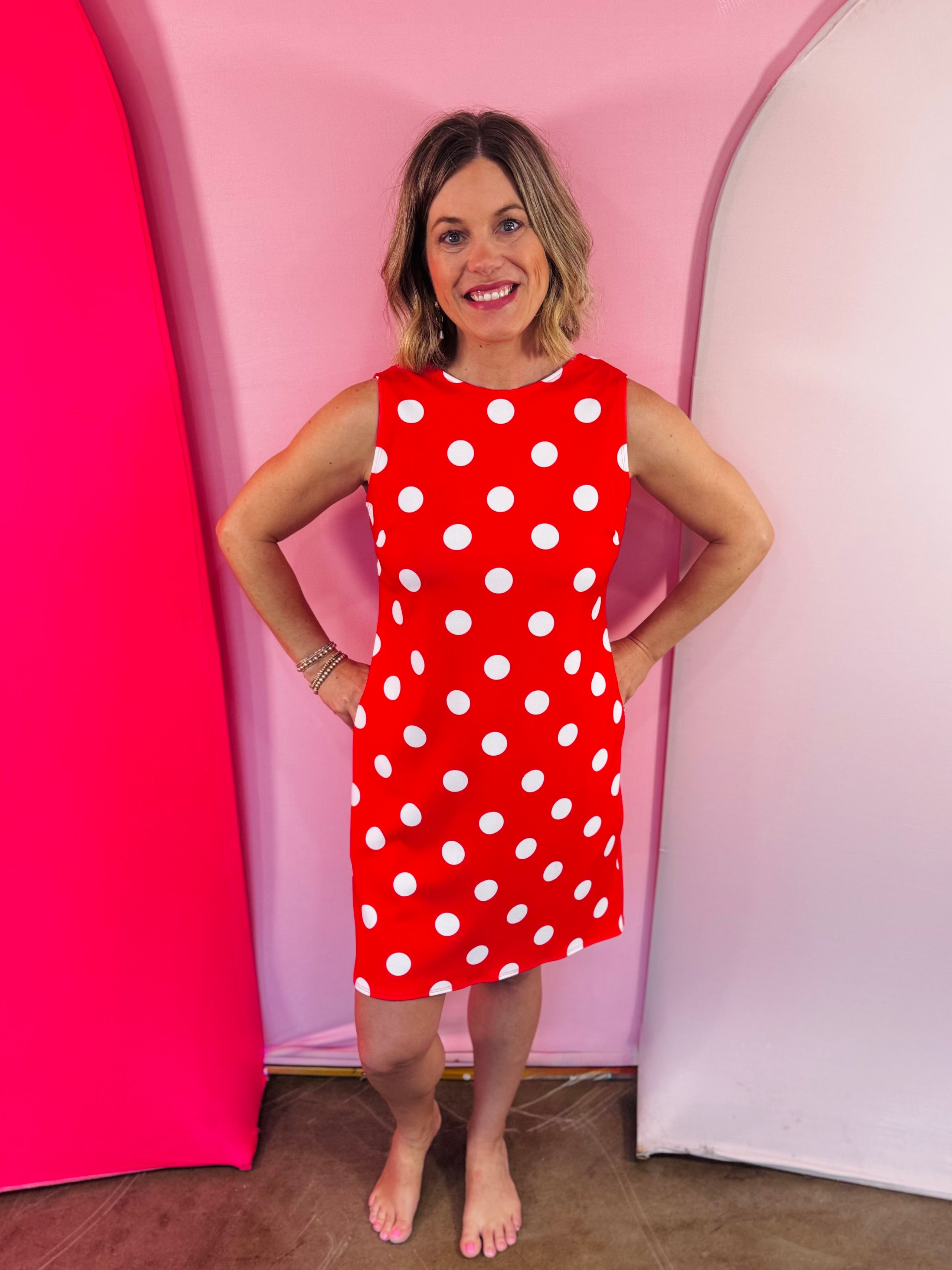 Red sleeveless polka dot dress with oversized bow back detail and side pockets.