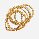 Gold beaded bracelet stack with multi-sized beads and clear rhinestone charm accent.