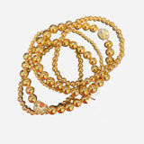 Gold beaded bracelet stack with multi-sized beads and clear rhinestone charm accent.