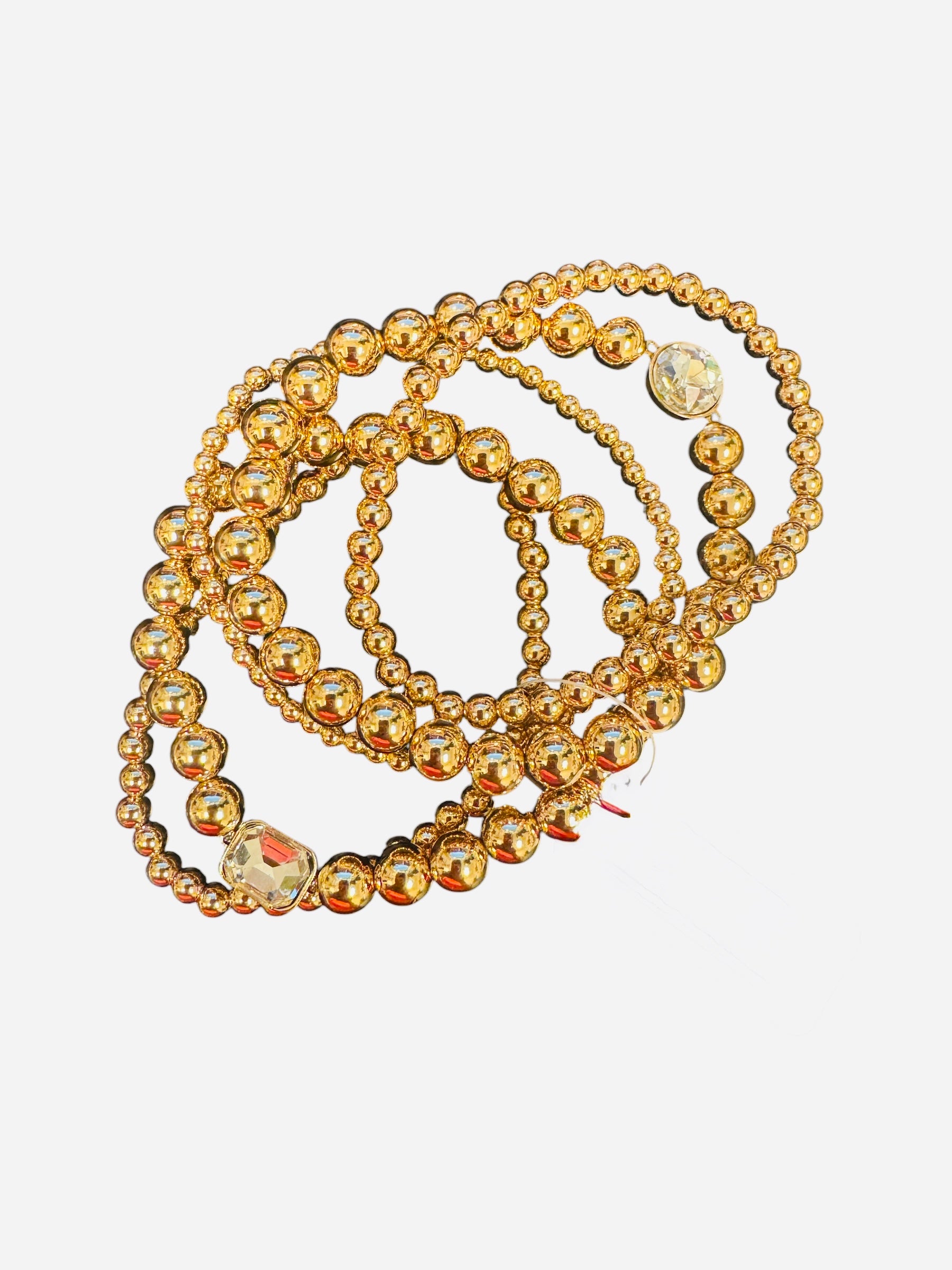 Gold beaded bracelet stack with multi-sized beads and clear rhinestone charm accent.