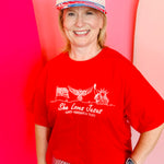 Red tee with She Loves Jesus and America Too white graphic and patriotic icons.