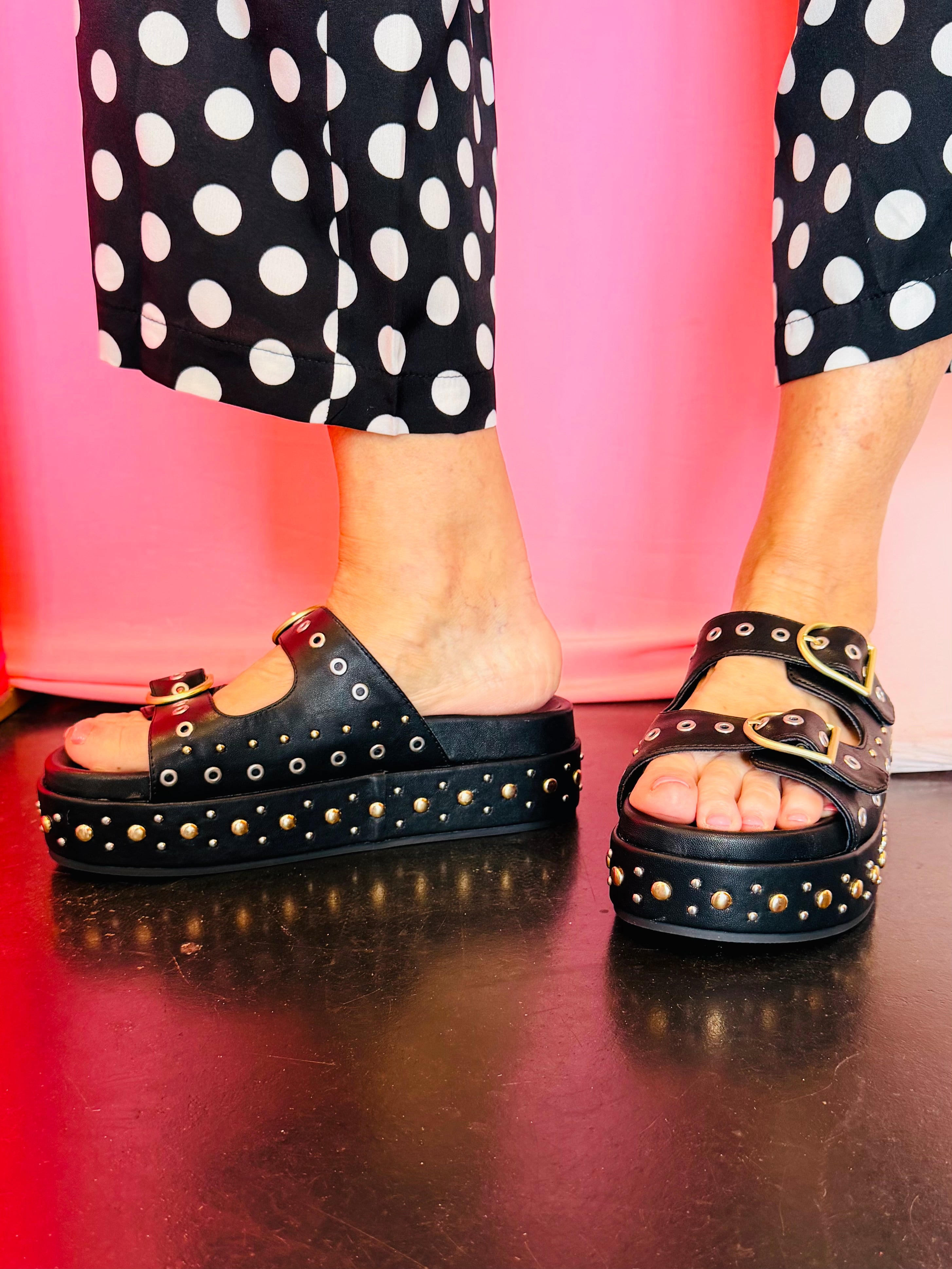 Black platform slide sandals with buckle straps and studded sole detail.