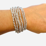 Set of seven silver water-resistant beaded bracelets with stretch fit for stylish stacking and comfort.