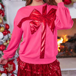 Pink sweatshirt with red sequin bow design, cozy fit, and festive holiday style.