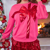 Pink sweatshirt with red sequin bow design, cozy fit, and festive holiday style.