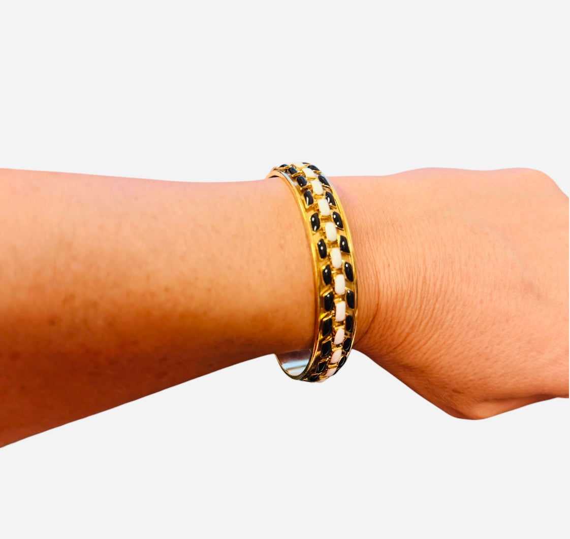 Gold-tone cuff bracelet with black and ivory enamel woven design.