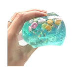 Blue cube squishy with glitter, seashells, and star accents inside.