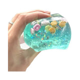 Blue cube squishy with glitter, seashells, and star accents inside.