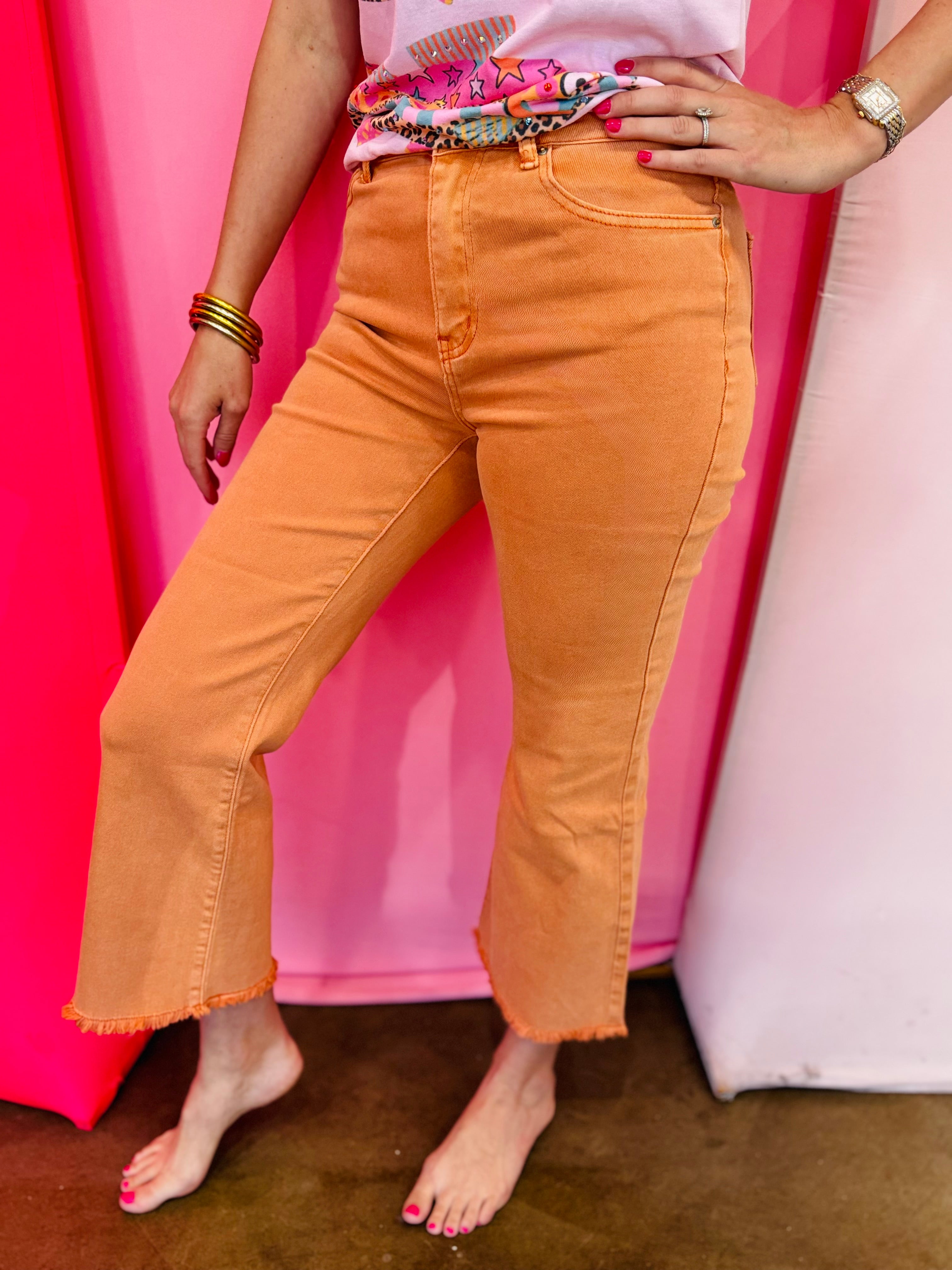 Orange cropped bootcut jeans with frayed hem and high-rise fit.