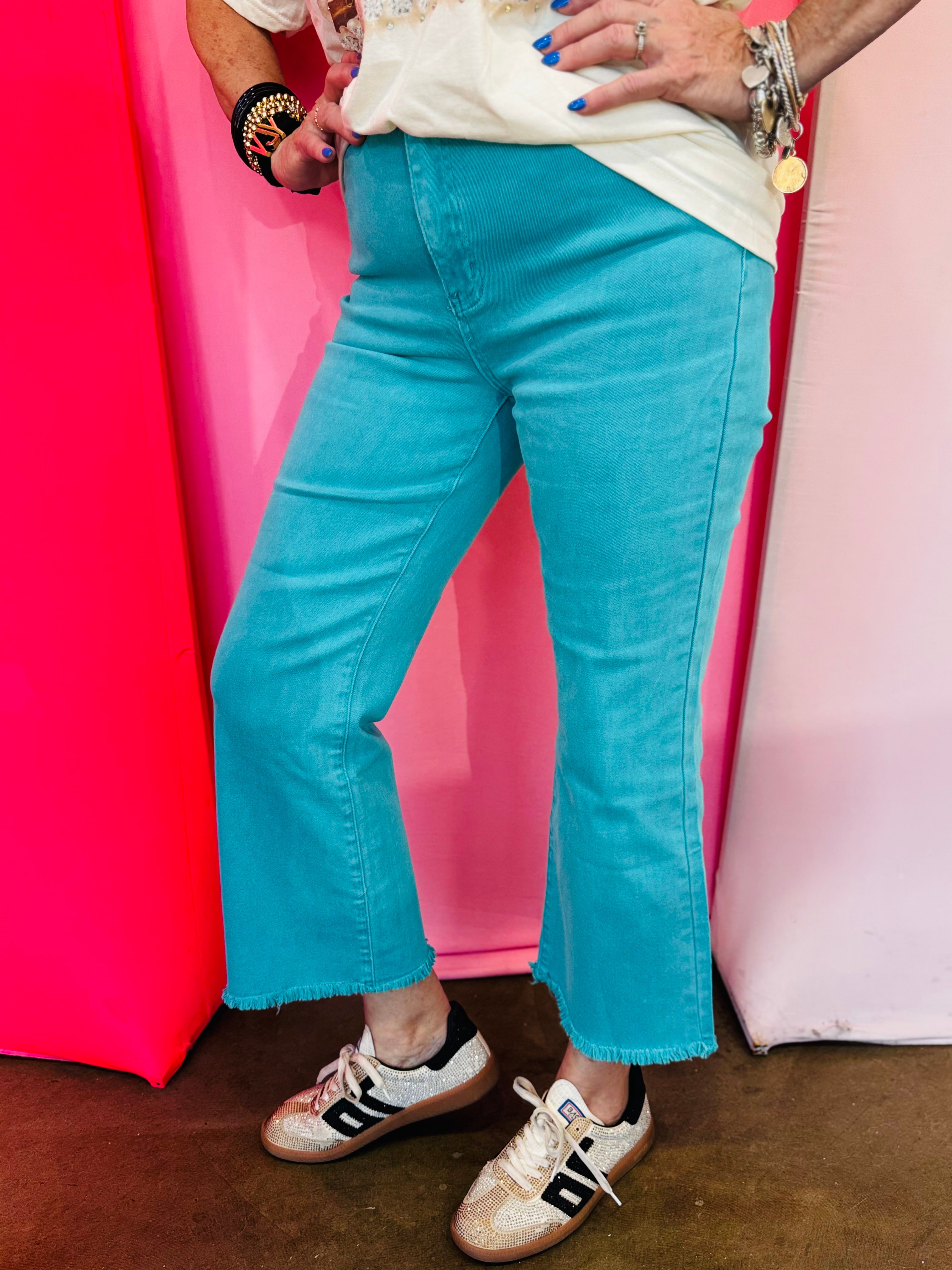 Turquoise cropped bootcut jeans with frayed hem and high-rise fit.
